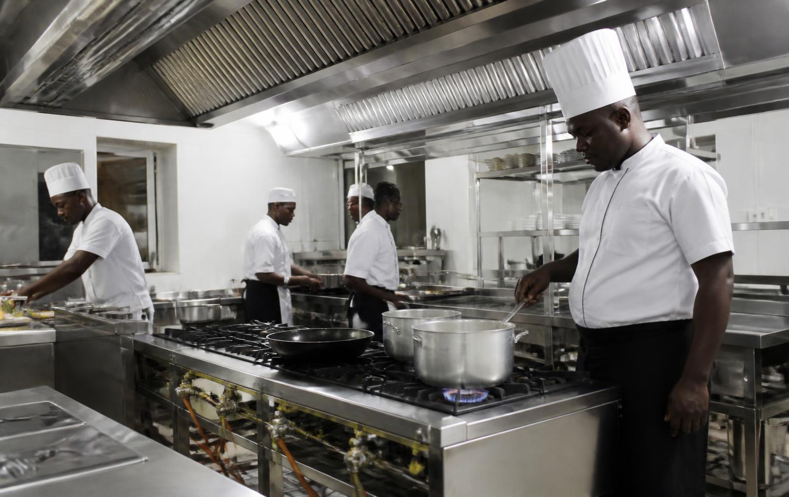 Stainless steel commercial kitchen with extraction hood and piped gas burners in a Ghanaian hotel